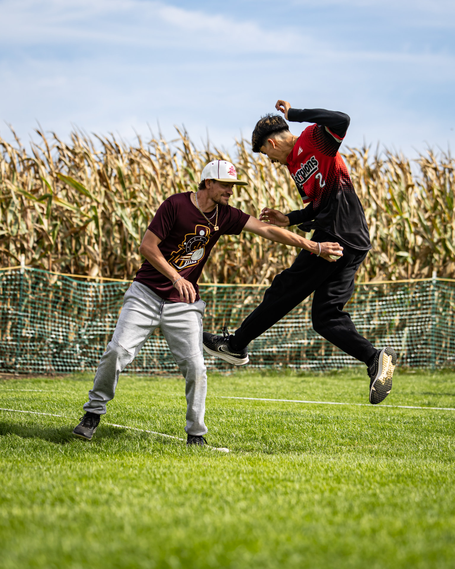 A runner leaping a tag in front of a cornfield
