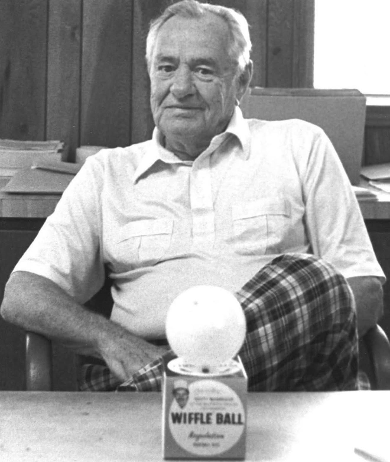 Archival black-and-white photo of a man at his desk with a boxed Wiffle Ball
