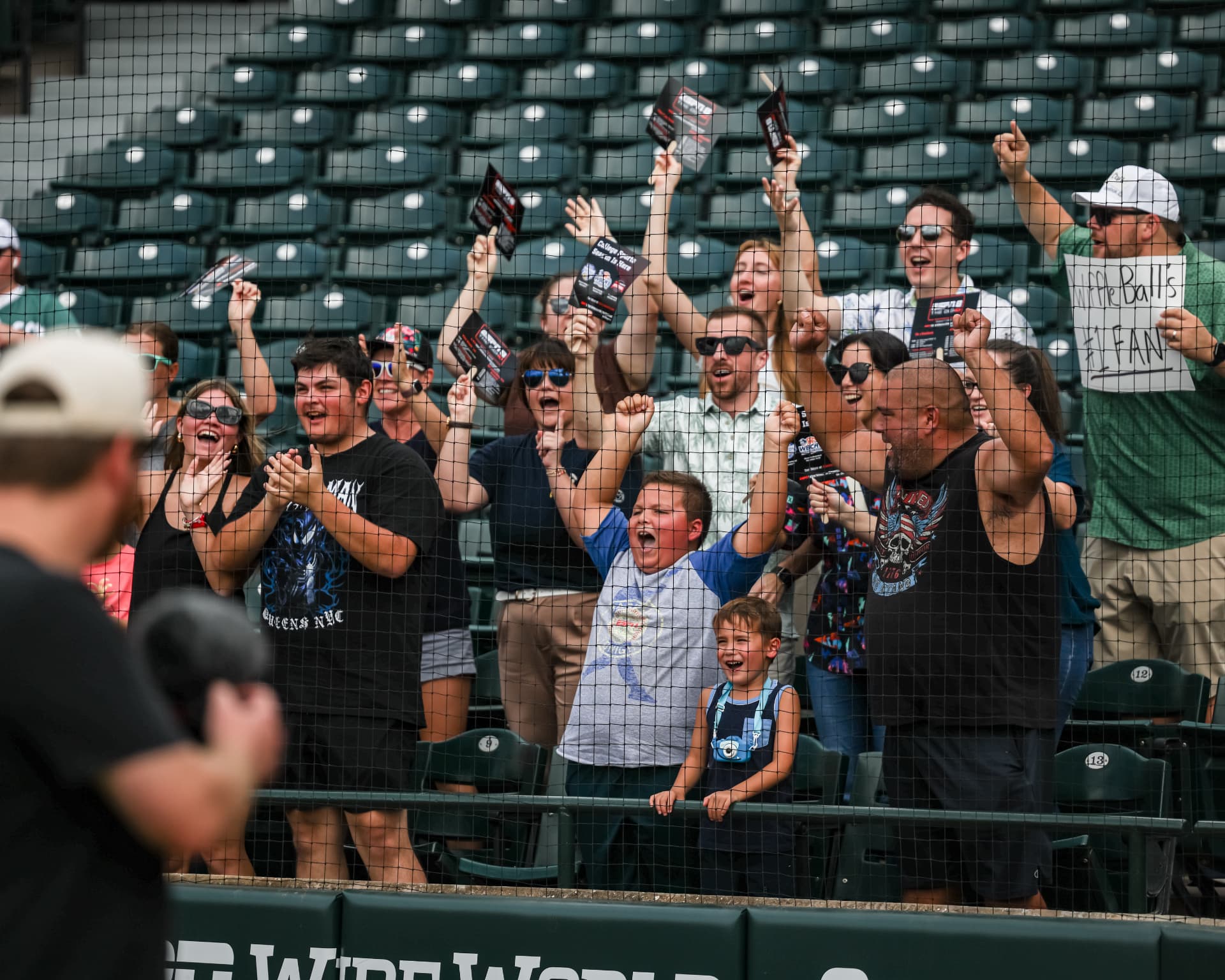 Fans cheering behind the netting at a Wiffle Ball game